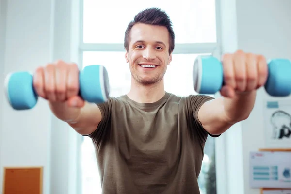 Feliz homem positivo segurando dois halteres azuis — Fotografia de Stock