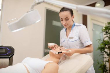 Dermatolog kadın yüzüne temizlik maskesi koyarak