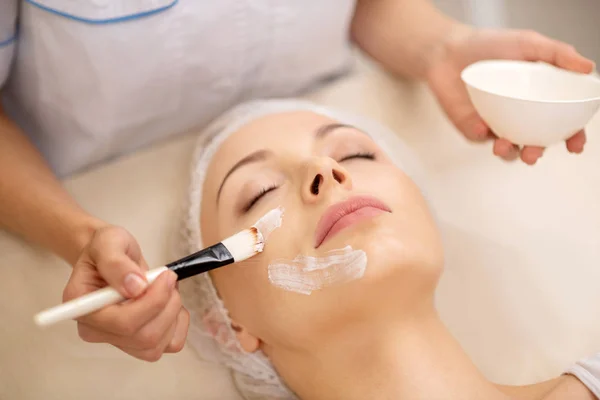 Dermatologista usando escova de cosméticos ao colocar máscara facial — Fotografia de Stock
