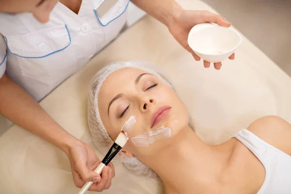 Cosmetologist putting cleansing face mask on client