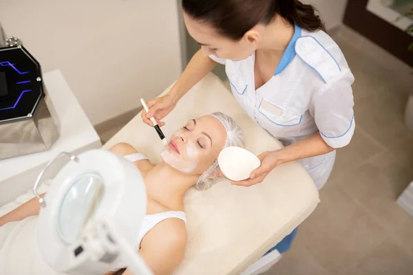 Cosmetologist colocando máscara de alginato no rosto de seu cliente — Fotografia de Stock