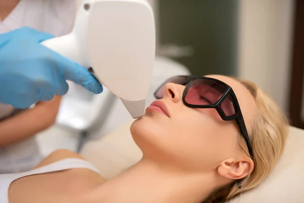 Blonde client wearing glasses having photo depilation of chin — Stock Photo, Image