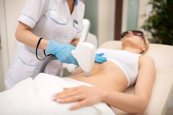 Depilatory master making laser depilation around navel of client — Stock Photo, Image