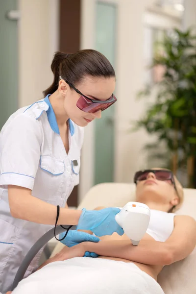 Depilatory master doing laser depilation on arms of client — Stock Photo, Image