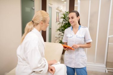 Koyu saçlı masaj uzmanı gülümseyerek ve müşteri sorular soran