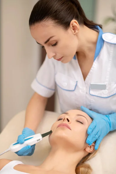 Dermatologista usando luvas azuis durante a limpeza da pele para o cliente — Fotografia de Stock