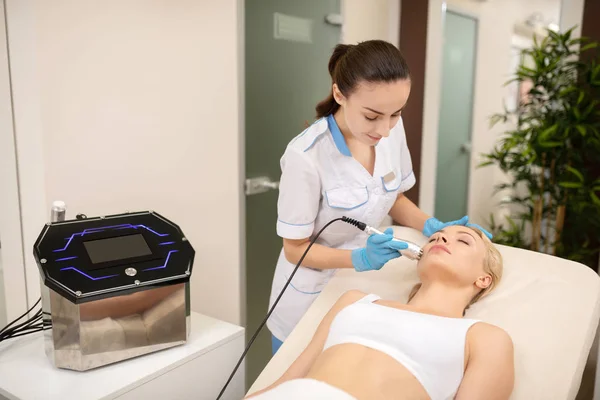 Dermatólogo de cabello oscuro haciendo tratamiento con láser para la piel del cliente — Foto de Stock