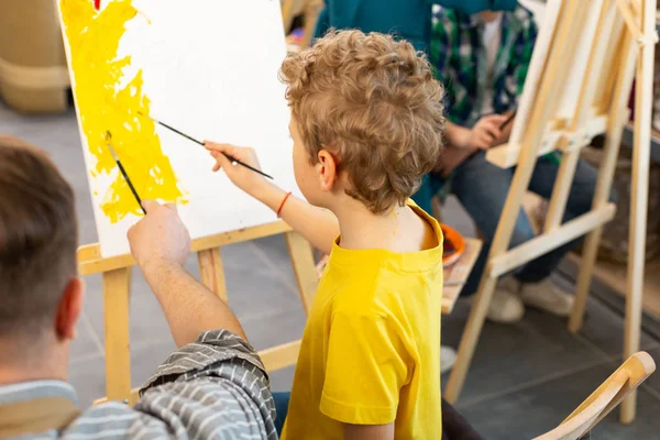 Menino segurando pintura escova colorir papel perto do professor — Fotografia de Stock
