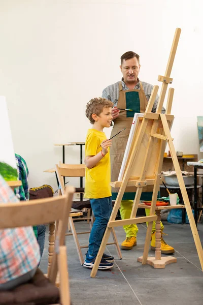Profesor de arte ayudando a su joven alumno creativo cerca del caballete de dibujo — Foto de Stock