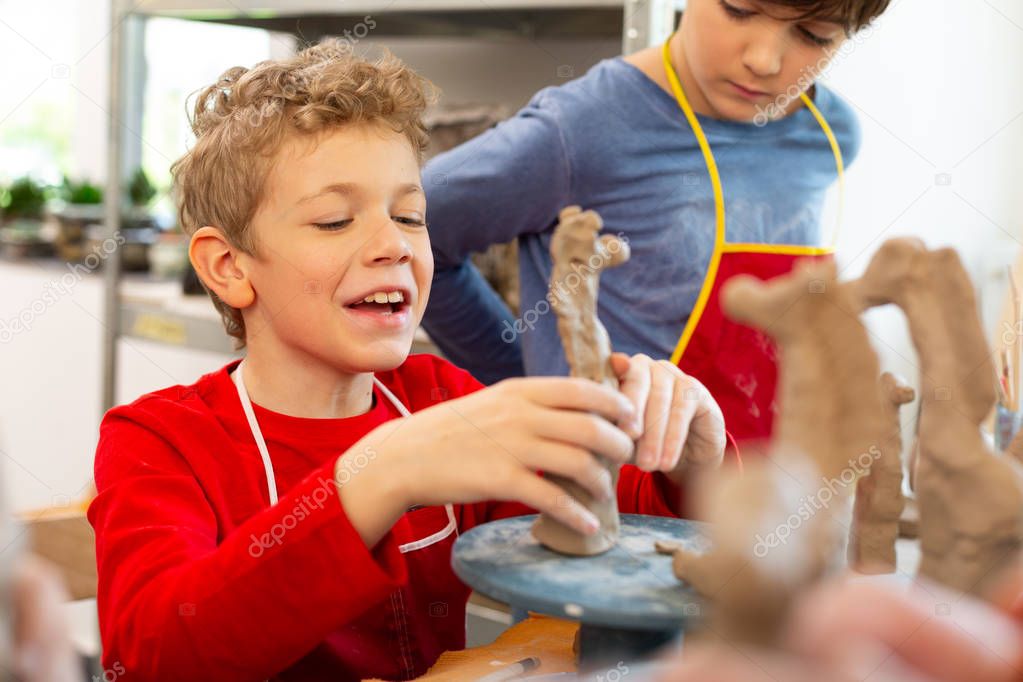 Boy laughing while modeling clay animals at art lesson