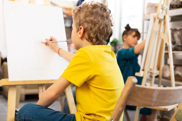 Schoolboy klädd i gul t-shirt teckning i konstskola — Stockfoto