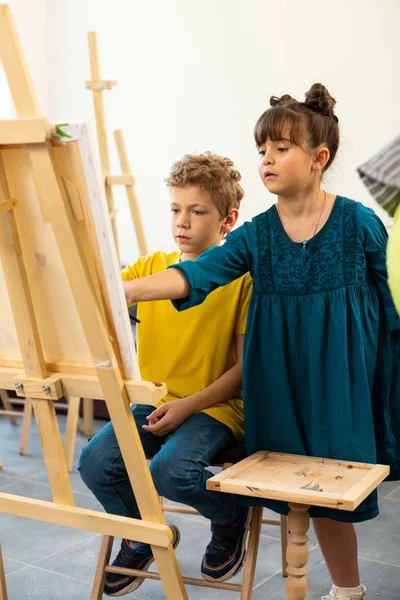 Söt tjej hjälper henne klasskamrat målning i konstskola — Stockfoto