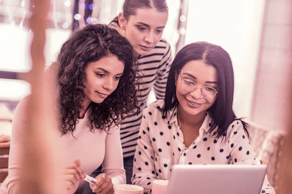 Three pleasant good-looking master students watching video on laptop together