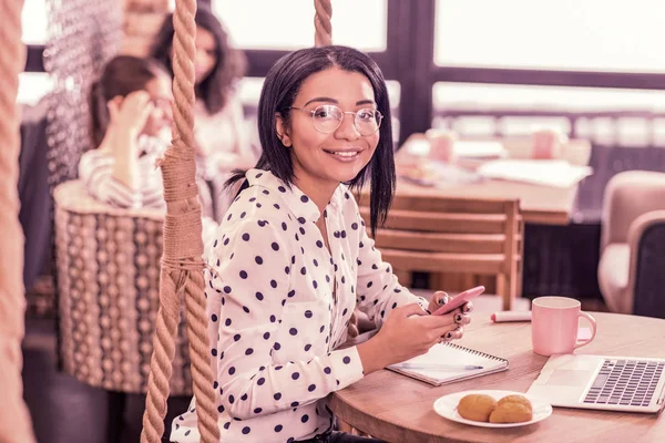 Mujer sonriente comiendo galletas y tomando té mientras espera a su novio en la cafetería — Foto de Stock
