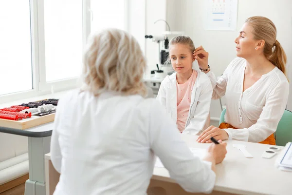 Cuidar a la madre de pelo largo visitando al médico con su hija — Foto de Stock