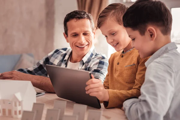 Two cute sons showing their photos to foster father on tablet