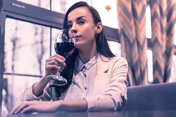 Tasty drink. Nice young woman holding a glass of wine while sitting in the restaurant