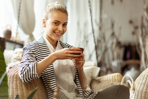 Senhora atraente com sorriso largo sorvendo chá quente de uma xícara — Fotografia de Stock