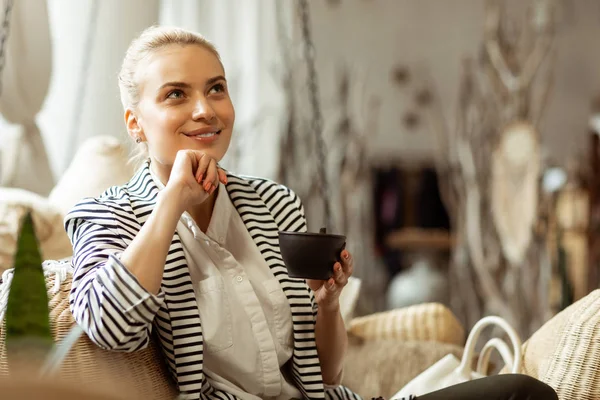 Pensativo mujer guapa con sonrisa suave sosteniendo taza de té negro — Foto de Stock