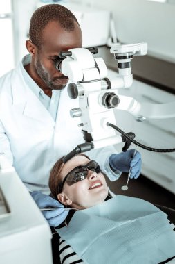 Seans sırasında özel makine kullanan ciddi koyu tenli diş hekimi