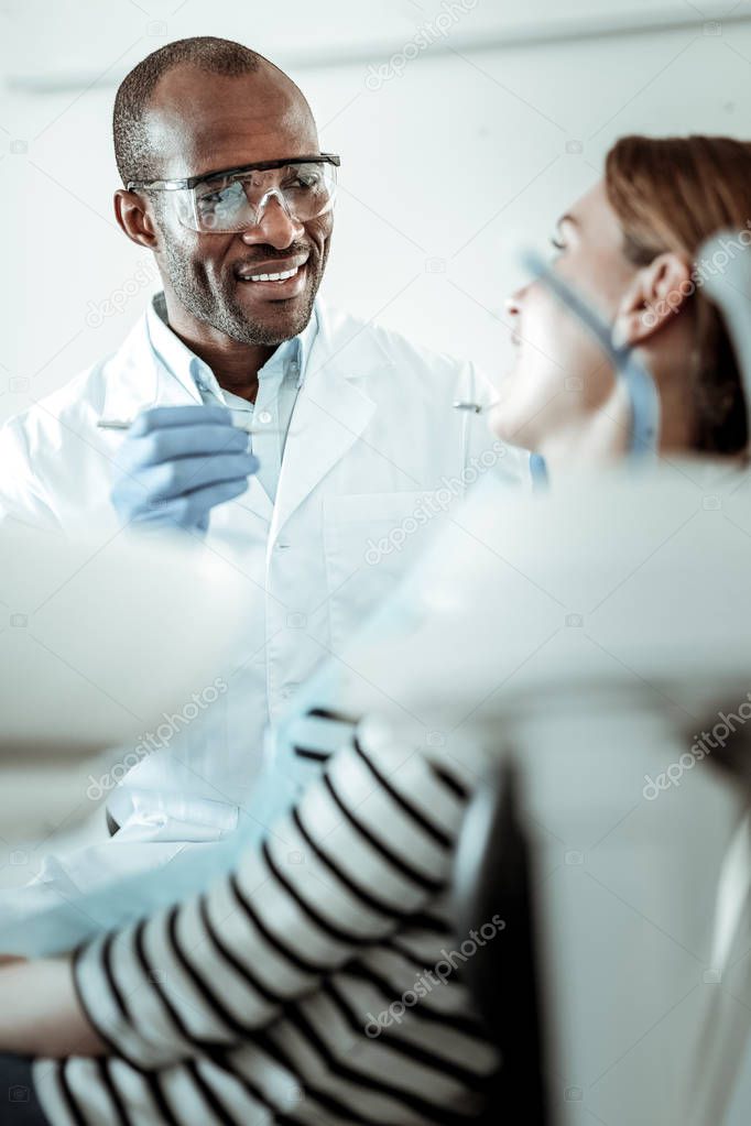 Professional dark-skinned dentist asking his patient about opening her mouth