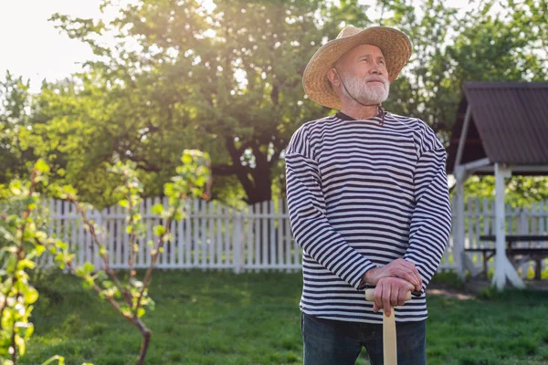 Grey-haired retired man holding shovel standing in his garden