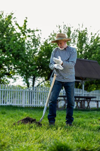 Hombre de pelo gris con guantes trabajando con pala en el jardín — Foto de Stock