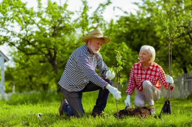 Kadın, kocasının ağaç dikmesini izlerken gülümsüyor.
