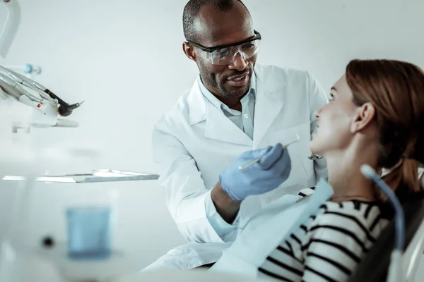 Médico de piel oscura concentrado curando sus dientes de paciente hembra — Foto de Stock