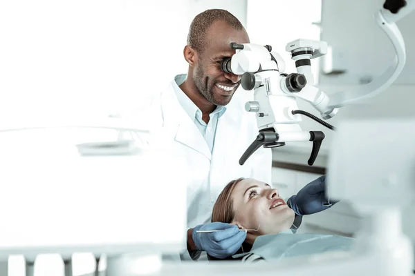 Médico de pele escura vestindo uniforme e olhando em microscópio especial — Fotografia de Stock