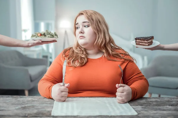 Negativ förtjust oversized flicka tittar på tallrik med sallad — Stockfoto