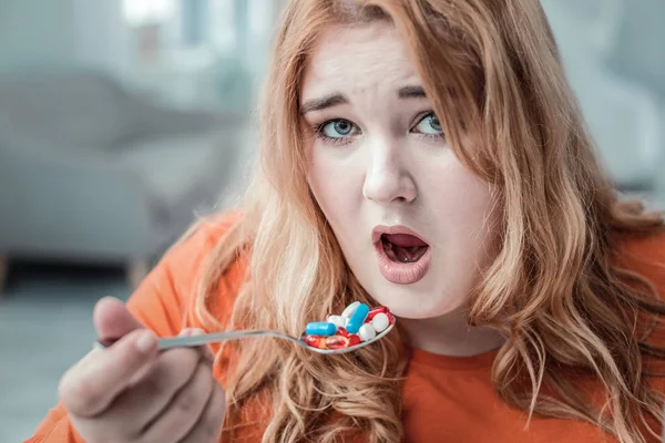 Эмоциональная пухлая женщина принимает витамины перед ужином — стоковое фото