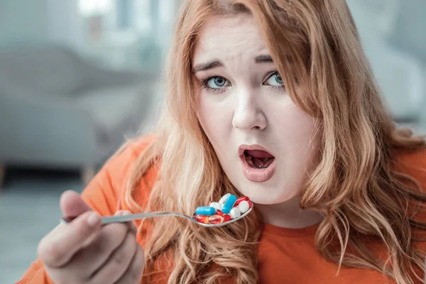 Emotional plump woman taking vitamins before dinner — Stock Photo, Image