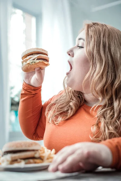 Ragazza paffuto aprendo la bocca mentre guardando hamburger — Foto Stock