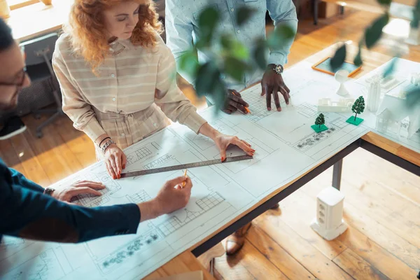 Krullend vrouw maken schetsen staande in de buurt van collega's — Stockfoto