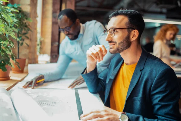 Diseñador de interiores barbudo sonriendo mientras trabaja cerca de colegas — Foto de Stock