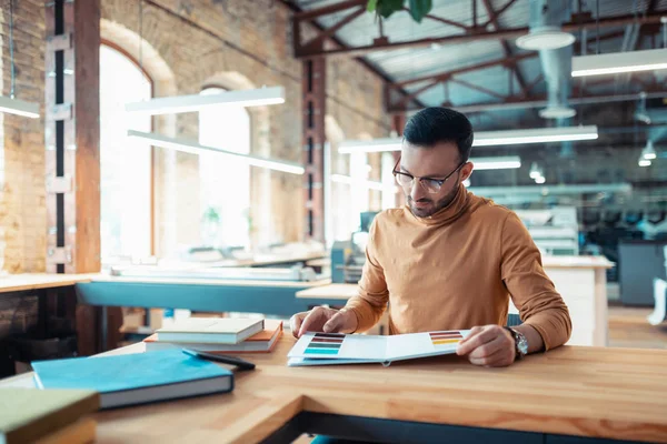 Writer sitting at the table and choosing color for book cover