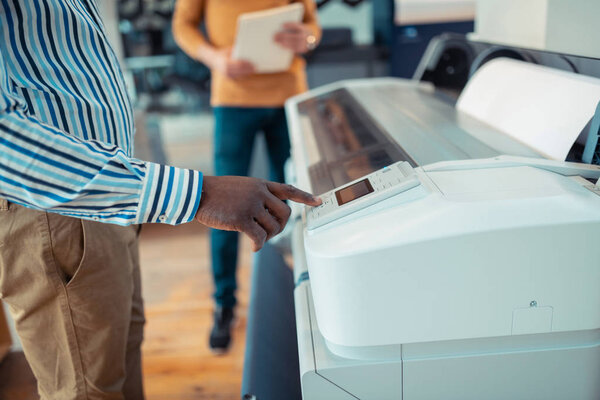 Close up of dark-skinned worker pressing button on printer
