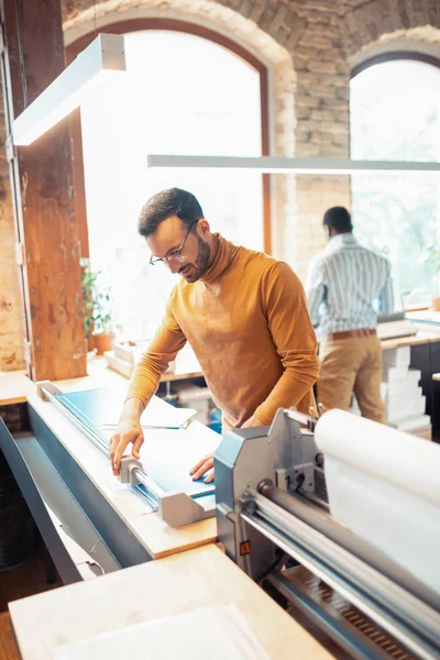 Man wearing orange polo working in big printing office