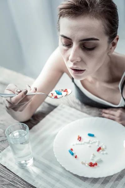 Concentrato bruna ragazza guardando cucchiaio con pillole — Foto Stock