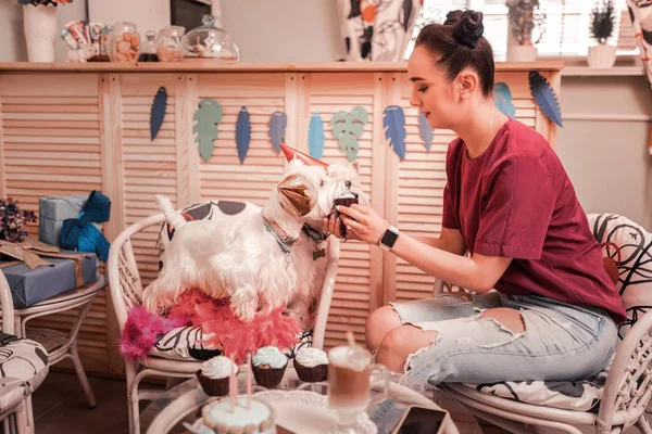 Woman wearing jeans feeding her dogs with cupcakes