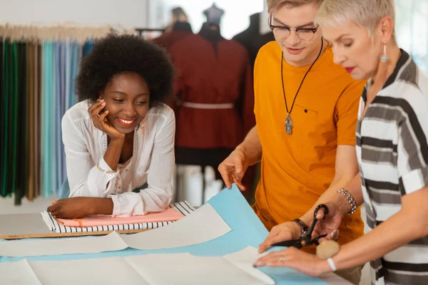 Sonriente joven diseñador de moda apoyado en la mesa — Foto de Stock