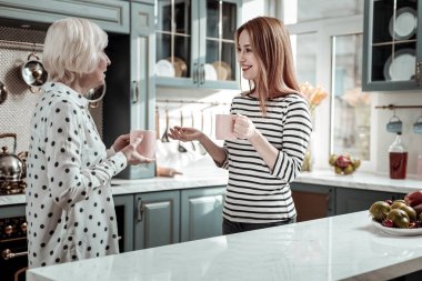 Mutfakta yaşlı annesiyle konuşurken gülümseyen genç kadın