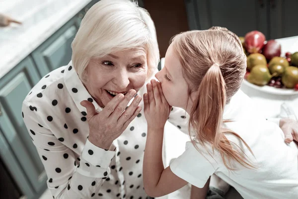 Emotionale Oma berührt ihren Mund, während kleines Mädchen Geheimnisse mit ihr teilt — Stockfoto