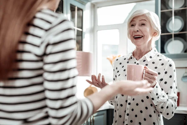 Emocional mujer mayor riendo mientras bebe té y habla —  Fotos de Stock