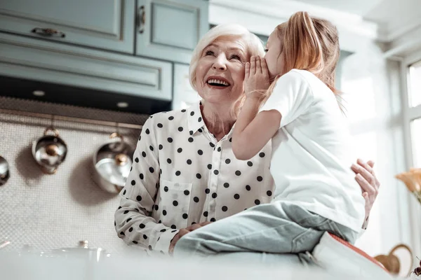 Happy Granny lyssnar på hemligheten med hennes barnbarn och leende — Stockfoto