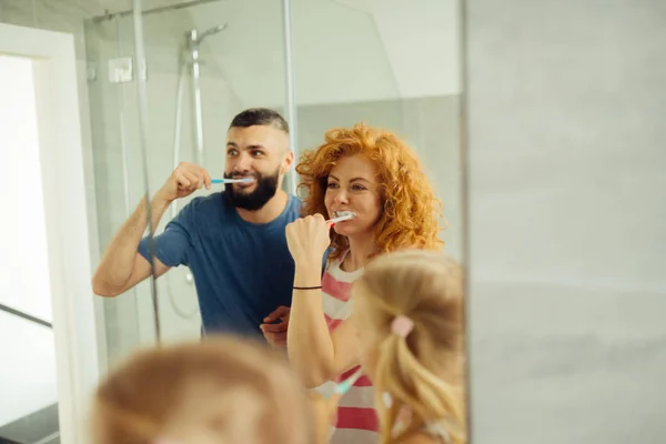 Alegre mujer pelirroja cepillándose los dientes junto con la familia — Foto de Stock