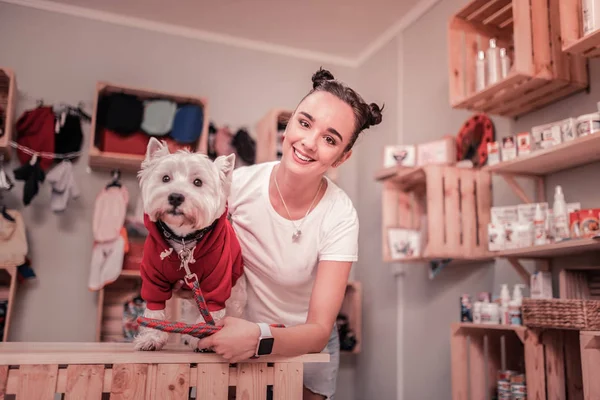 Dunkelhaarige Frau lächelt, nachdem sie Hund rote Kleidung angezogen hat — Stockfoto