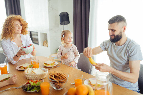 Радостный бородатый мужчина чистит банан в руке
