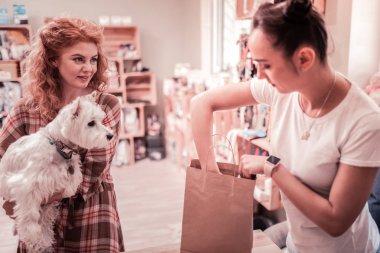Alışveriş yaparken onu beyaz kabarık köpek tutan kıvırcık kadın